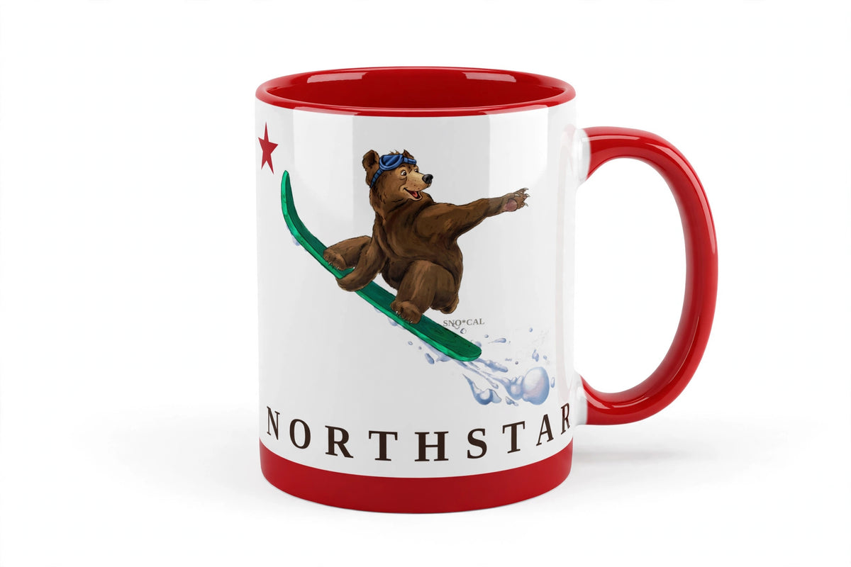 White ceramic mug with red rim handle and inside with Northstar CA flag design, grizzly bear catching air on a snowboard, angled view